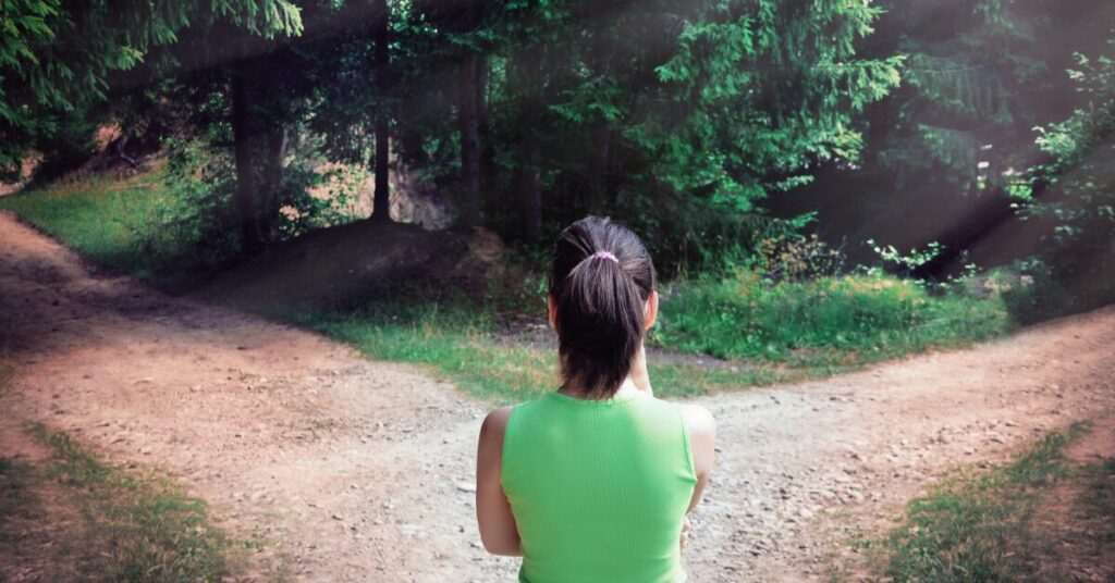 Woman standing at a fork in a forest path, symbolizing the decision between passive and nonpassive real estate activities for tax purposes.