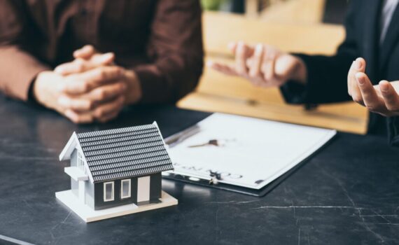 Two people discussing real estate investment strategy with a model house and contract on the table.